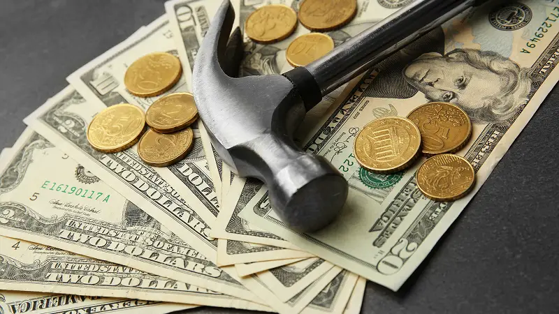 Hammer resting on dollar bills and coins, representing expensive home repairs for seniors on a fixed income.